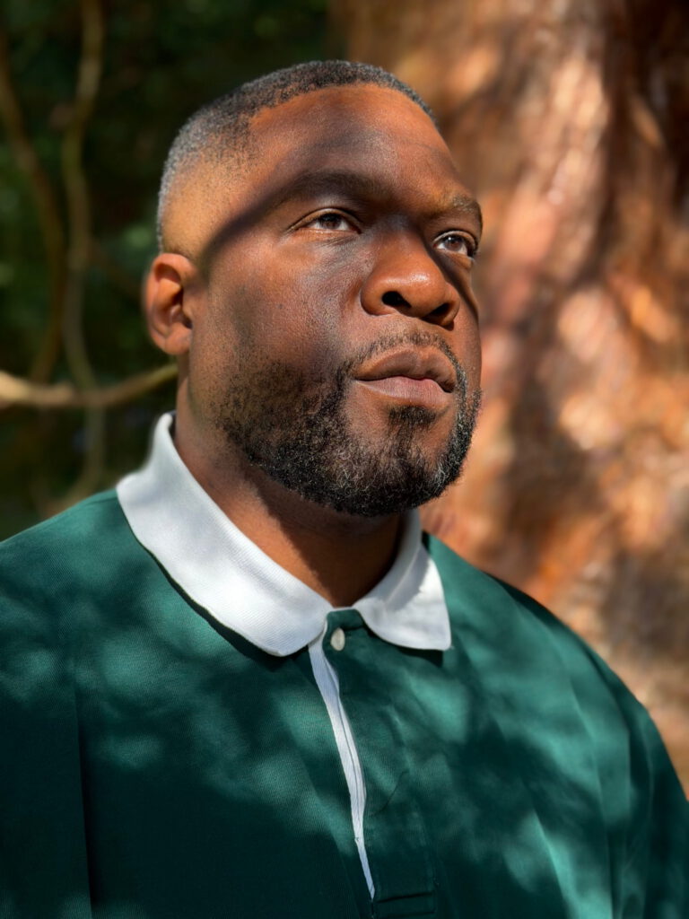 Nike Oruh outdoors in dappled sunlight, looking up, in a green rugby shirt