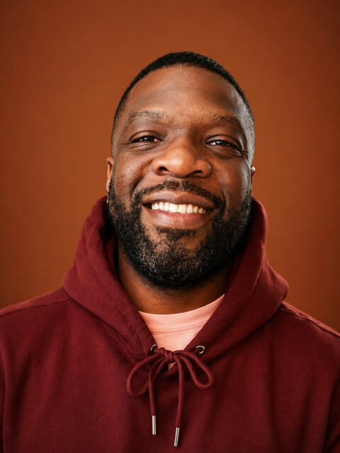 Nike Oruh smiling, in a maroon hoodie against a warm orange background